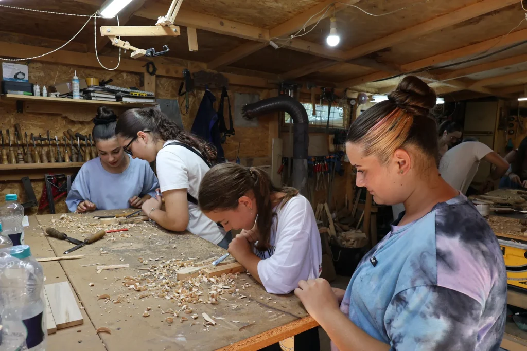 Tineri la atelier de cioplit lemn, lucrând la bancul de lucru plin de așchii