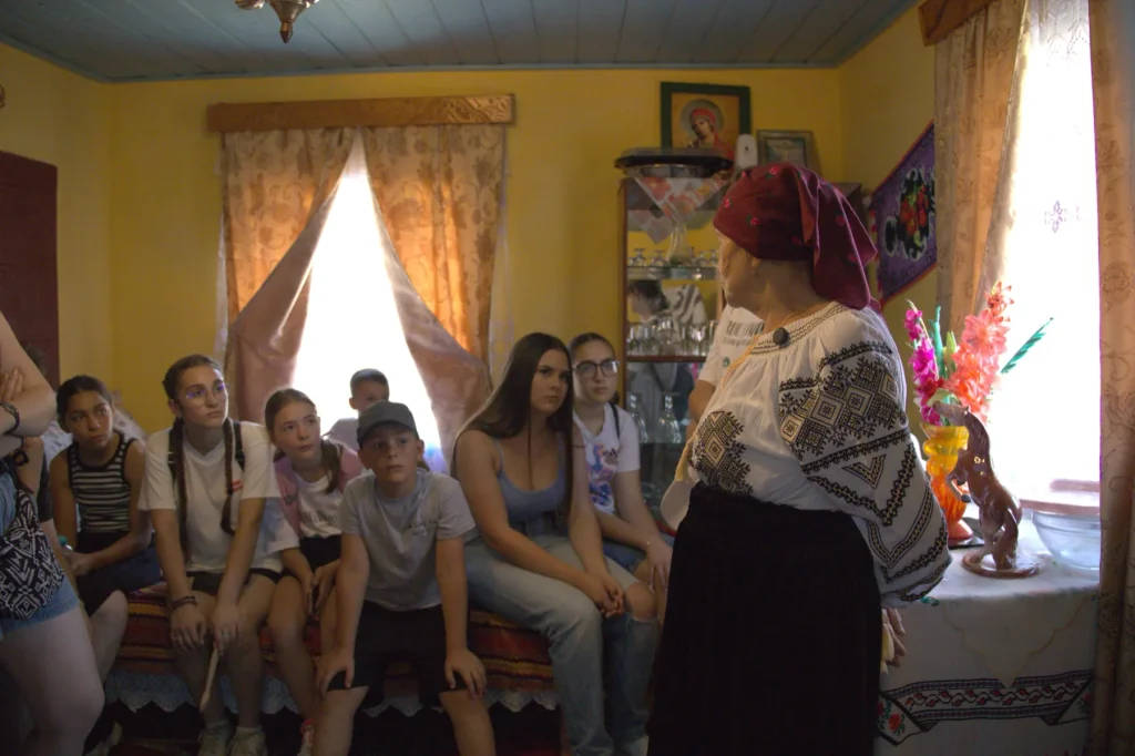 Gazda în costum popular povestind unui grup de copii în camera bună de la Casa Veronica