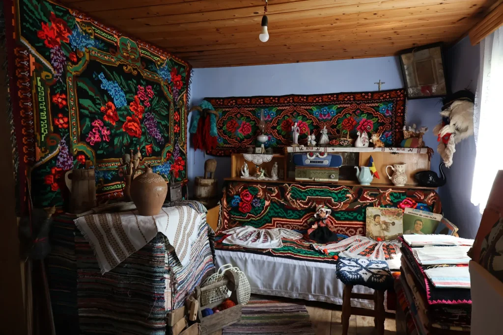 Interiorul Muzeului Satului Rotunda, cu scoarțe înflorate, laviță și obiecte gospodărești vechi