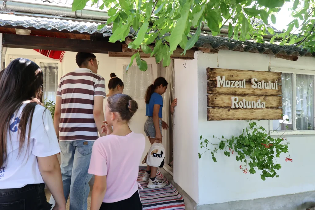 Vizitatori la intrarea în Muzeul Satului Rotunda, lângă firma de lemn